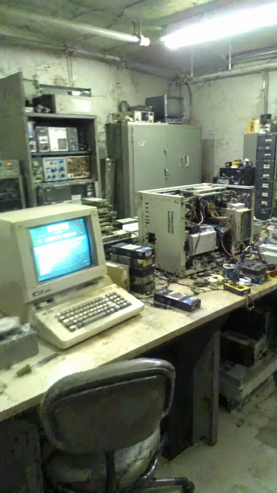 A cluttered basement lab with a beige computer terminal, 1983